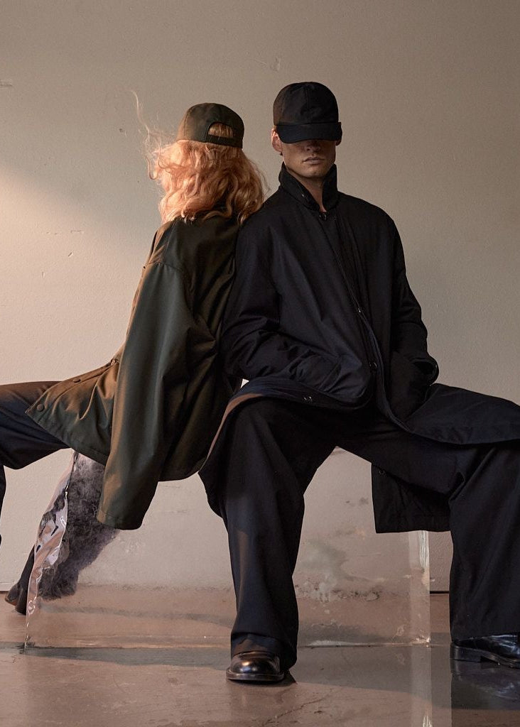 Two people sitting on a bench against a plain wall in AUTER Shirt Jacket.