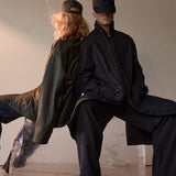 Two people sitting on a bench against a plain wall in AUTER Shirt Jacket. 