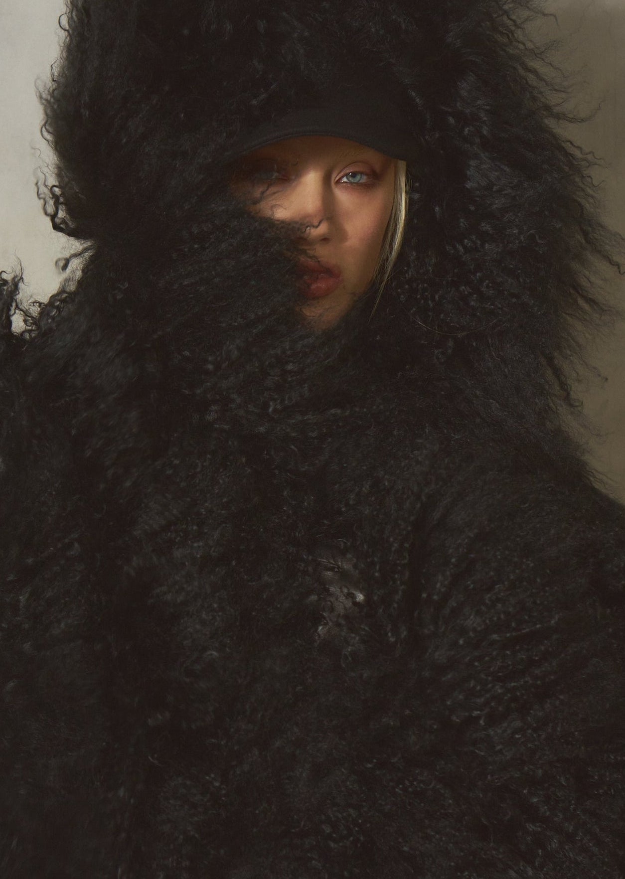 A female model wearing an oversized black fur hooded coat, posed against a plain light wall. The face is partially obscured by the dense black texture.