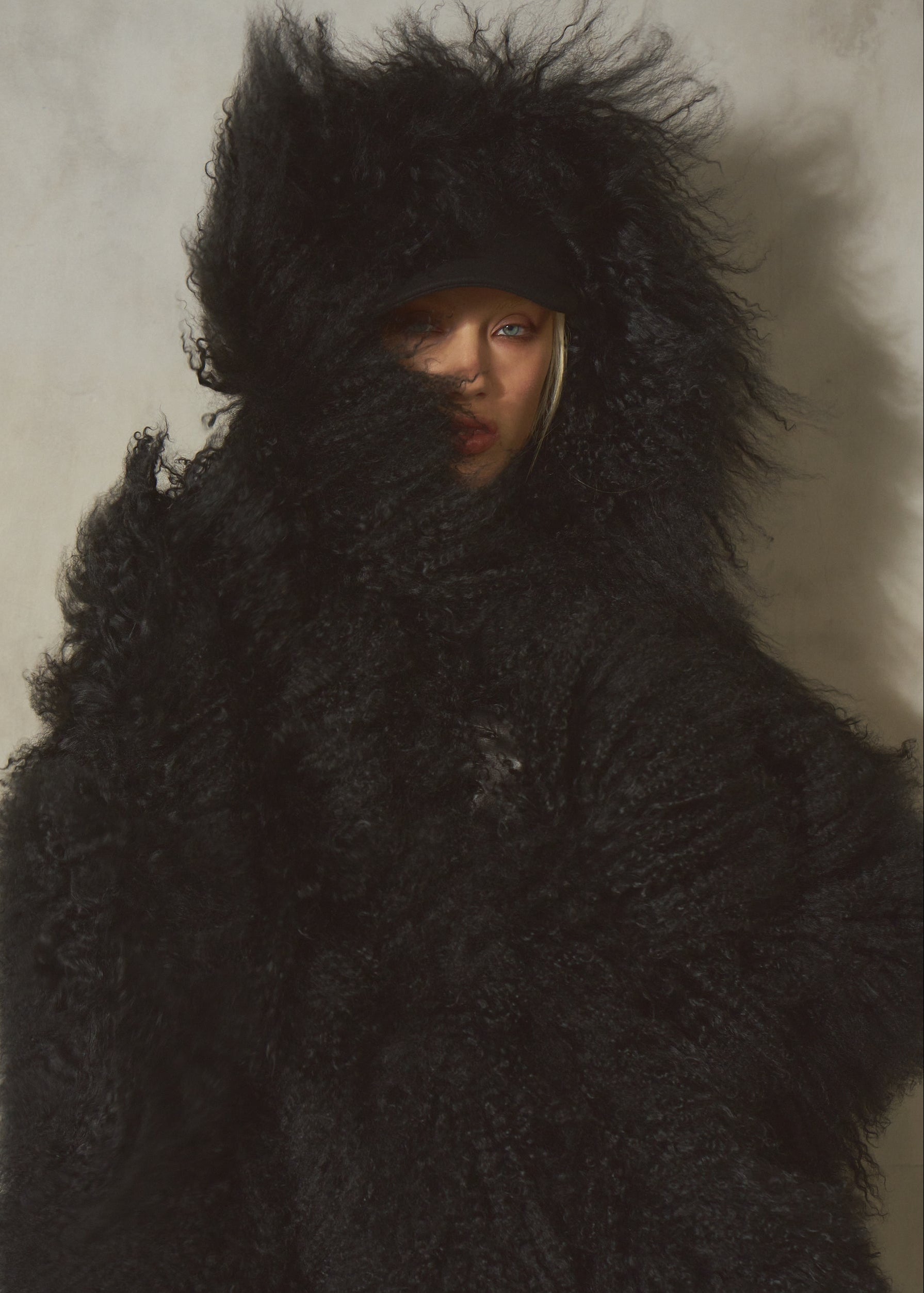A female model wearing an oversized black fur hooded coat, posed against a plain light wall. The face is partially obscured by the dense black texture.