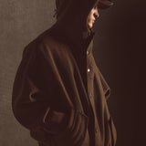 Model wearing an dark olive hooded coat against a dark background