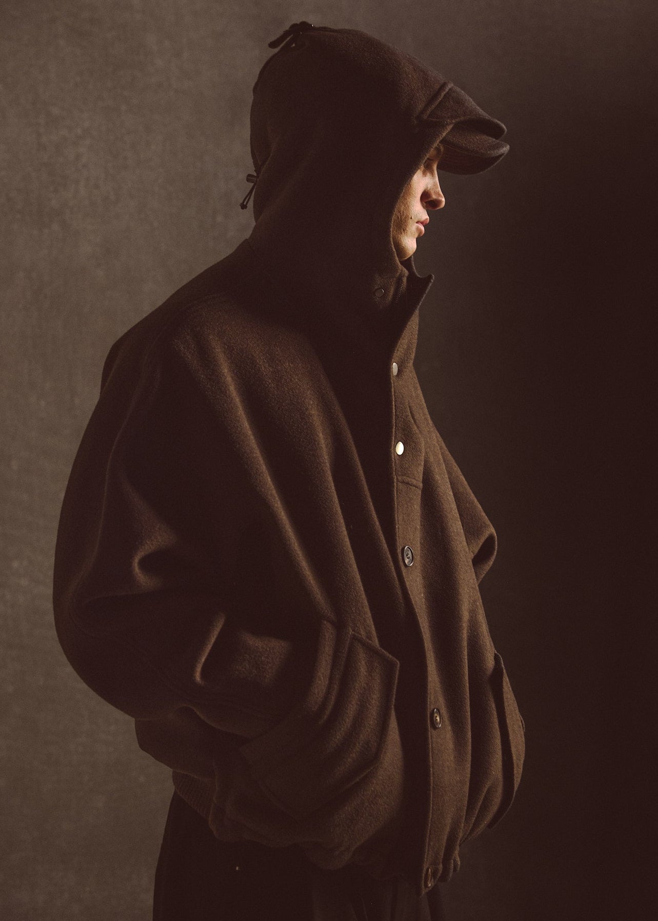 Model wearing an dark olive hooded coat against a dark background