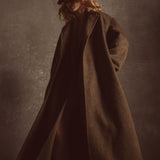 Model wearing a long brown coat and hat against a dark background