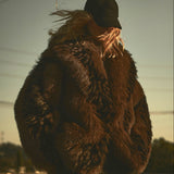 Model wearing a brown and black faux fur jacket with a black wool cap. 