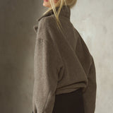 A woman wearing a loose, oversized taupe-brown herringbone pullover jacket and black wide-leg pants.