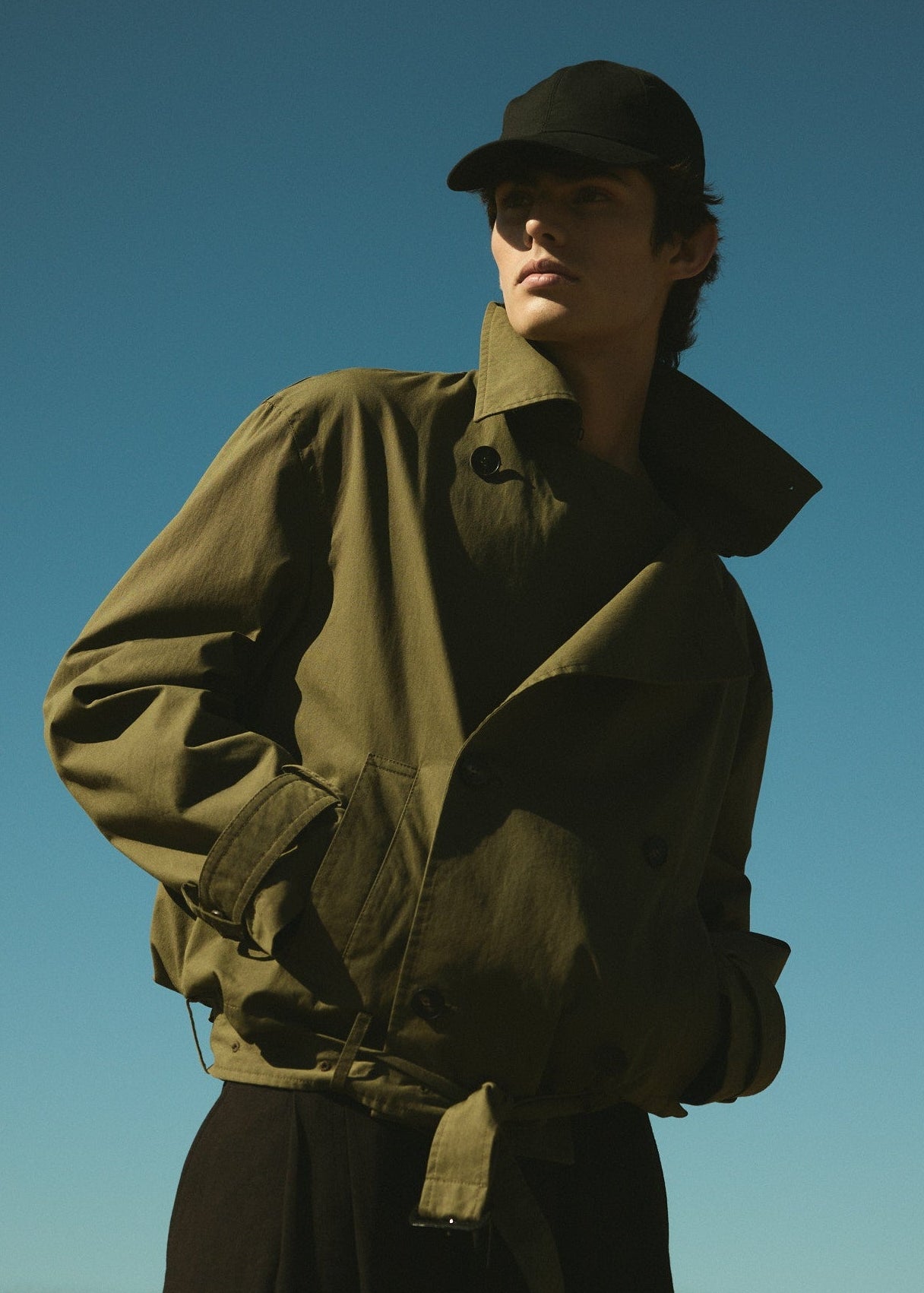 Man wearing a green jacket and cap against a clear blue sky