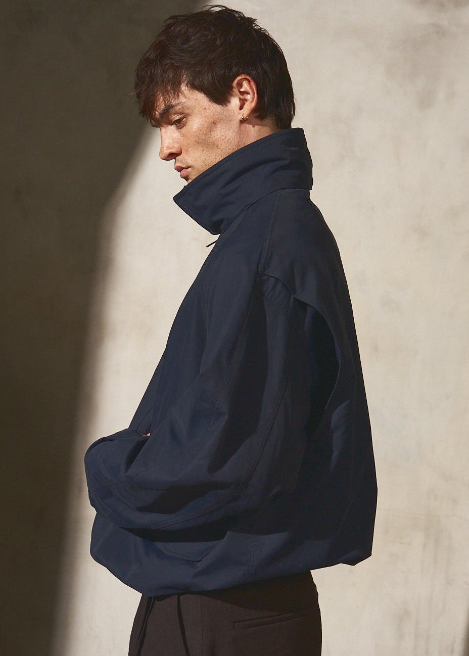Man wearing a dark blue jacket against a plain wall